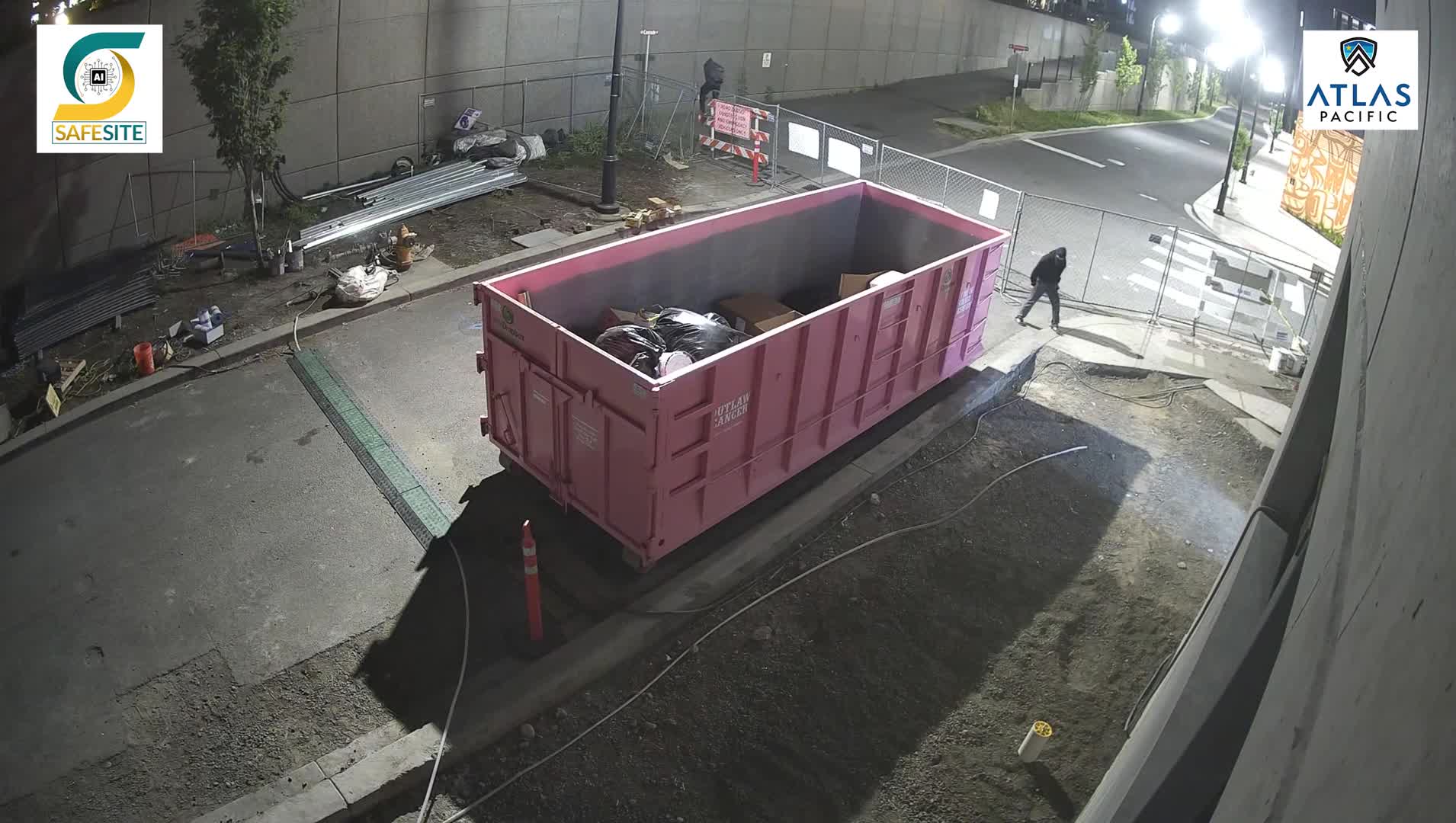 Nighttime camera footage of a person beside a construction-site dumpster
